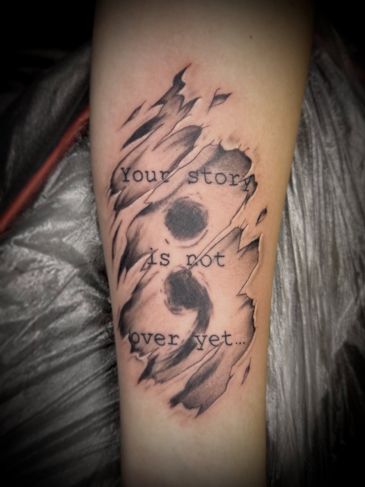 Semicolon tattoo on a forearm with text saying Your story is not over yet