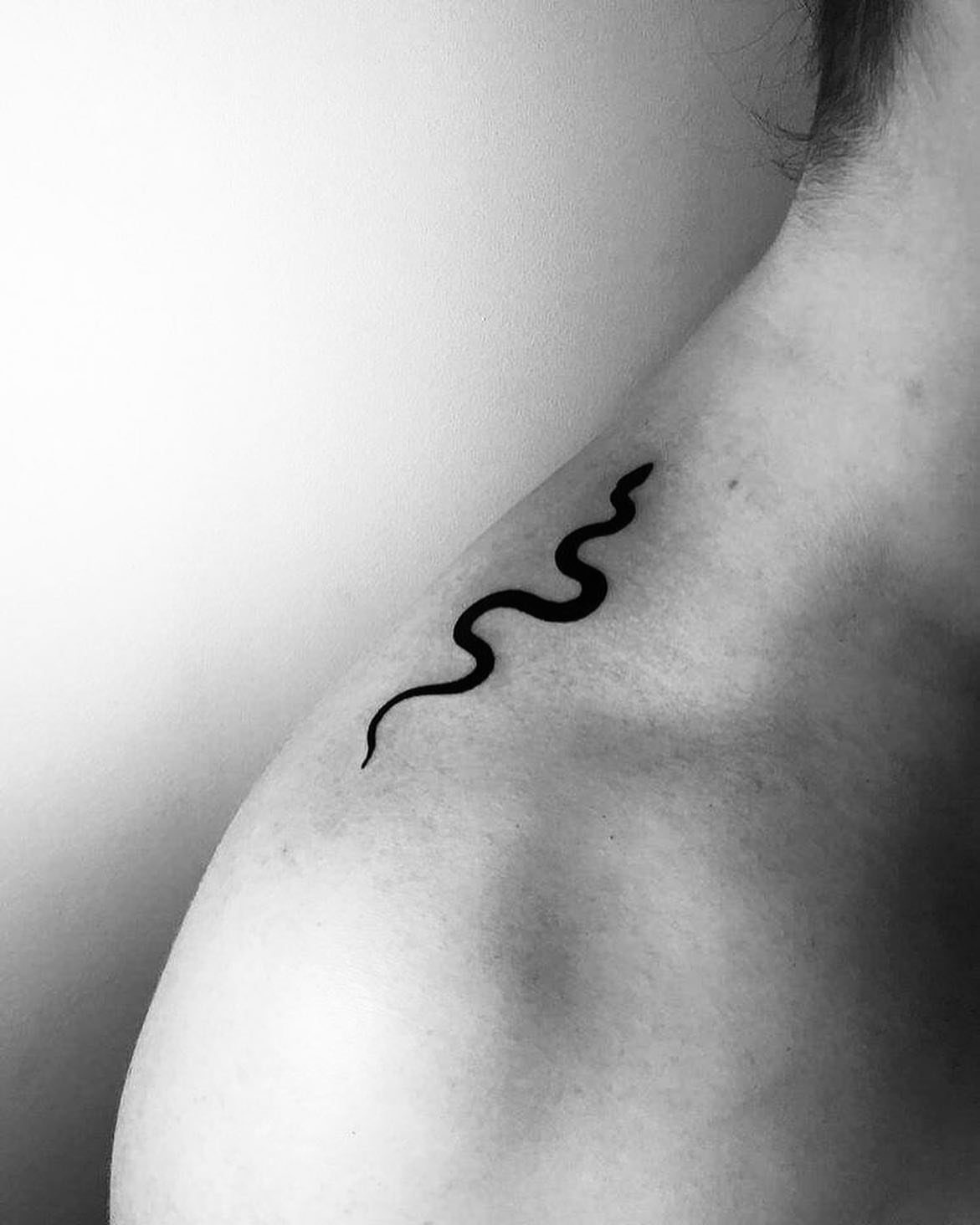 Minimalist black snake tattoo winding across a person's shoulder and upper back.