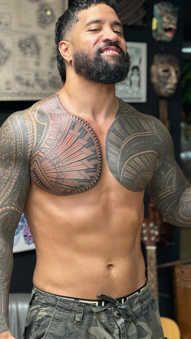 Man with extensive tribal tattoos on his chest and arms posing shirtless.