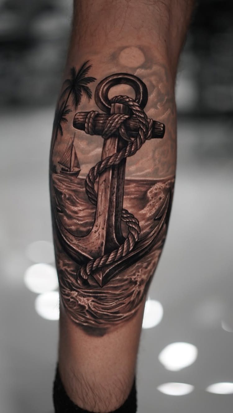 Detailed anchor tattoo with rope, sailboat, and palm tree on a forearm.