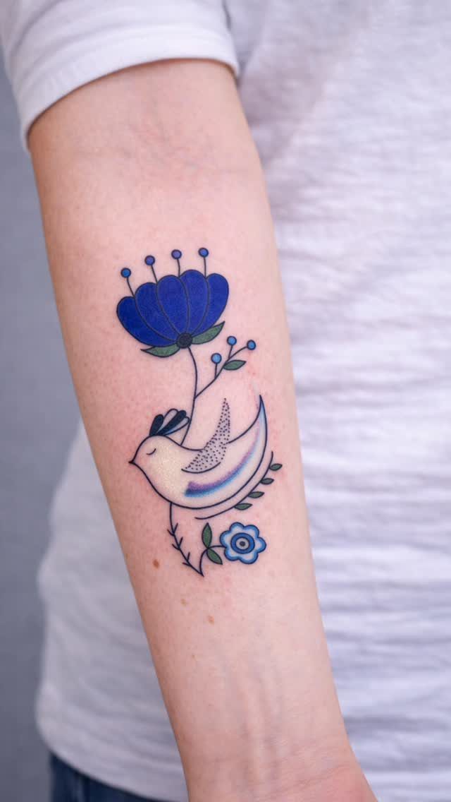 Stylized white bird tattoo with blue flowers on a person's forearm