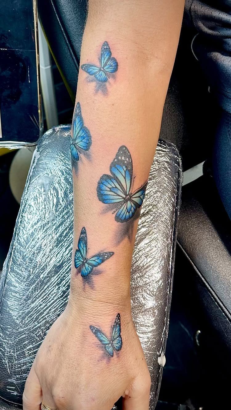 Blue butterfly tattoos with 3D shading on a person's forearm and wrist.
