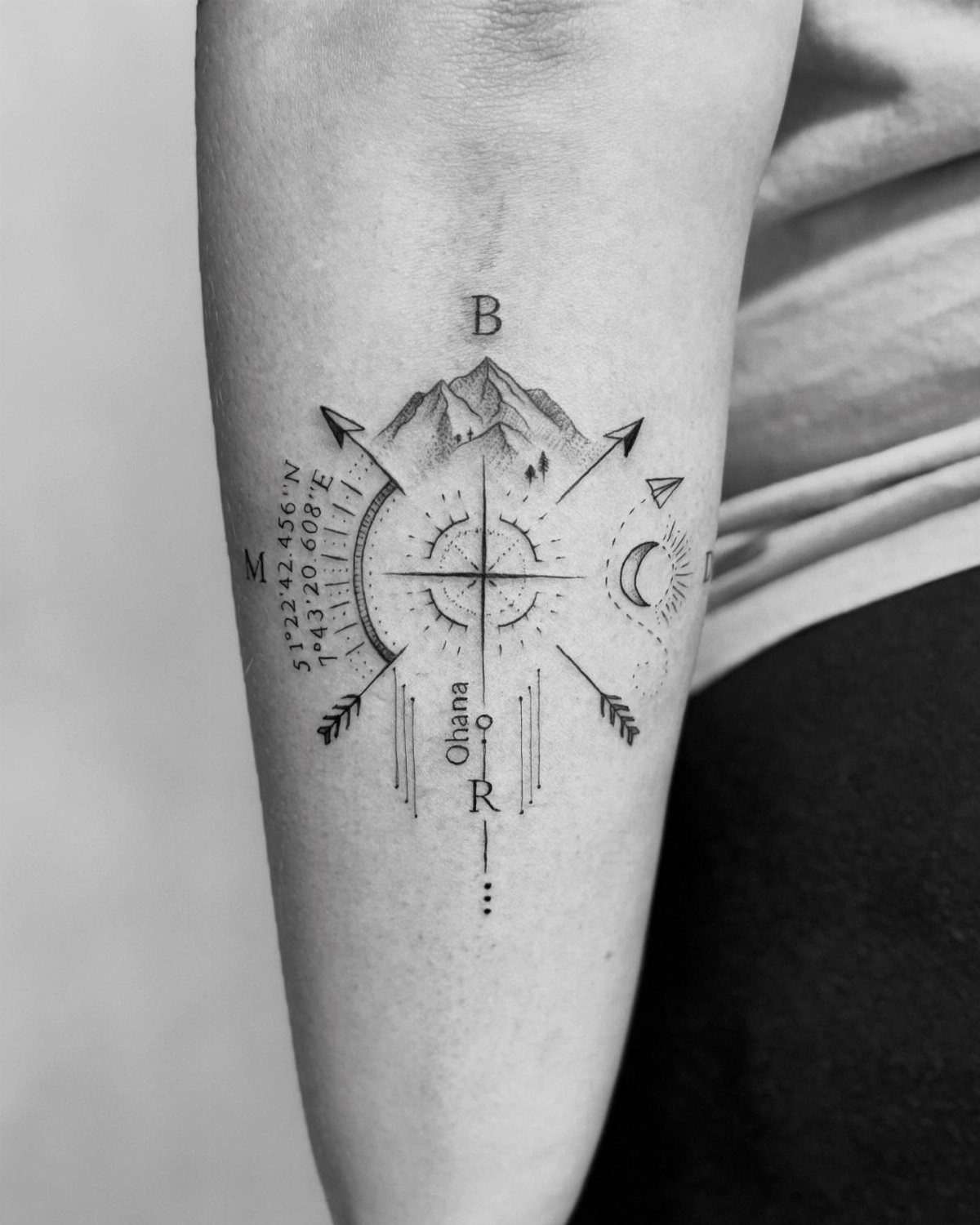 Compass rose tattoo with mountains and coordinates on a person's forearm