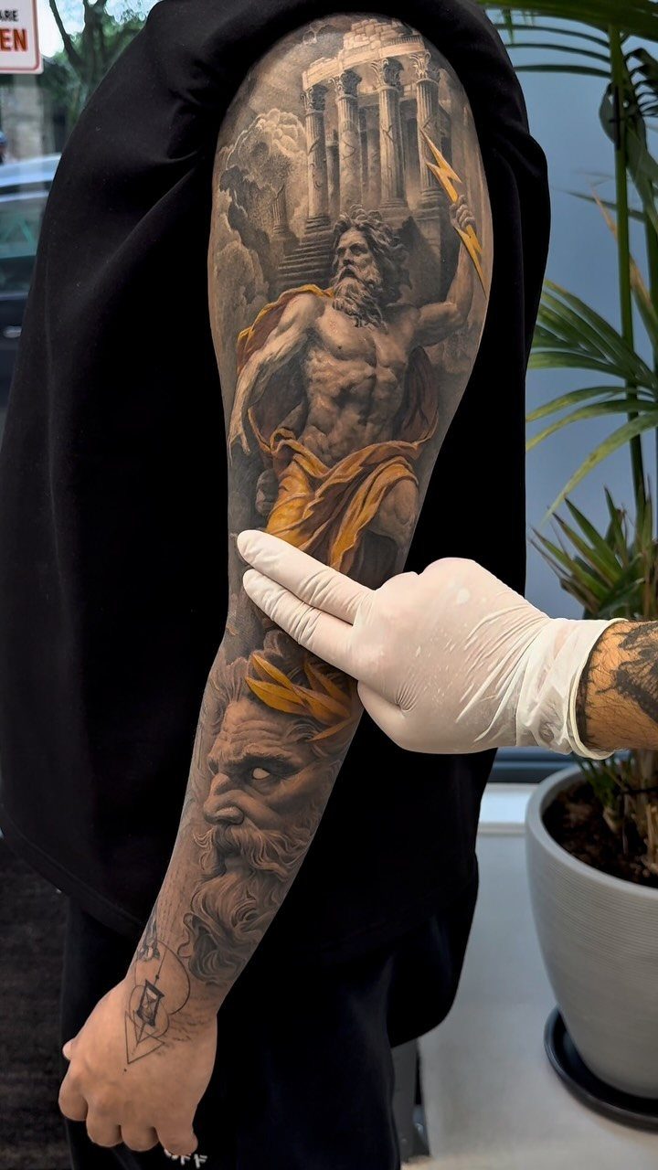 Detailed sleeve tattoo of a muscular man and Greek architecture on an arm.