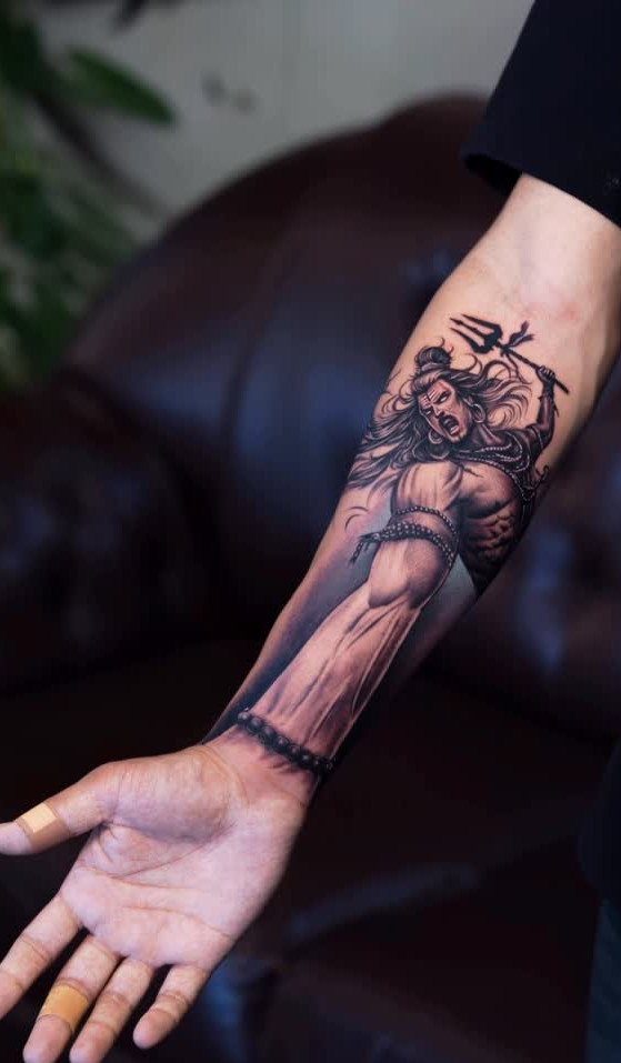 Detailed black and grey forearm tattoo of a deity holding a trident.