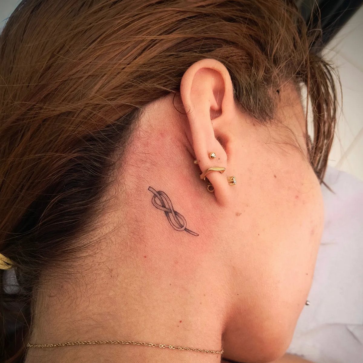 Knotted rope tattoo on the side of a person's neck near the ear.