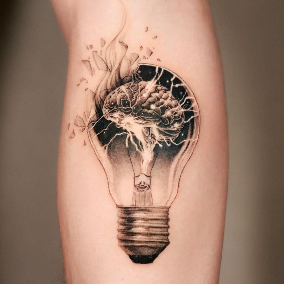 Lightbulb tattoo with a human brain inside and shattered glass on skin