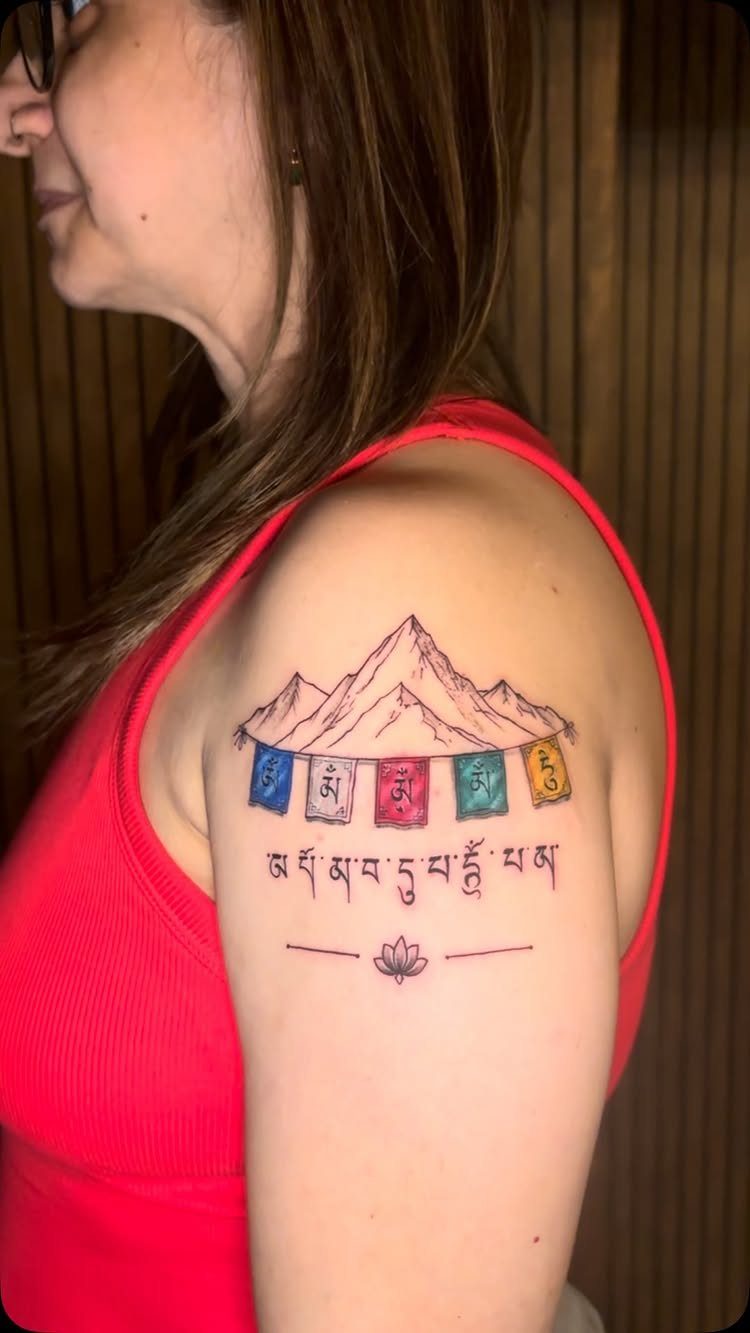 Tattoo on an arm showing a mountain, prayer flags, and a small lotus flower.