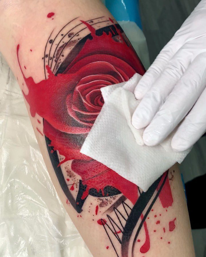 Red rose tattoo with black geometric accents being wiped clean by a gloved hand