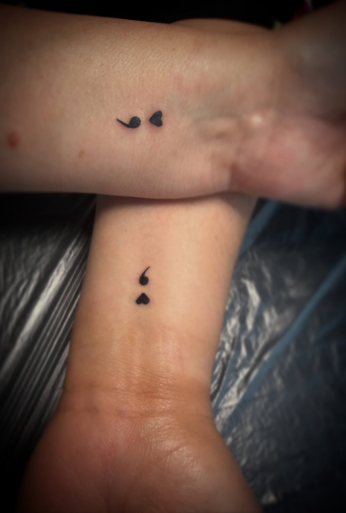Semicolon tattoos on two wrists, with the dots replaced by small black hearts.