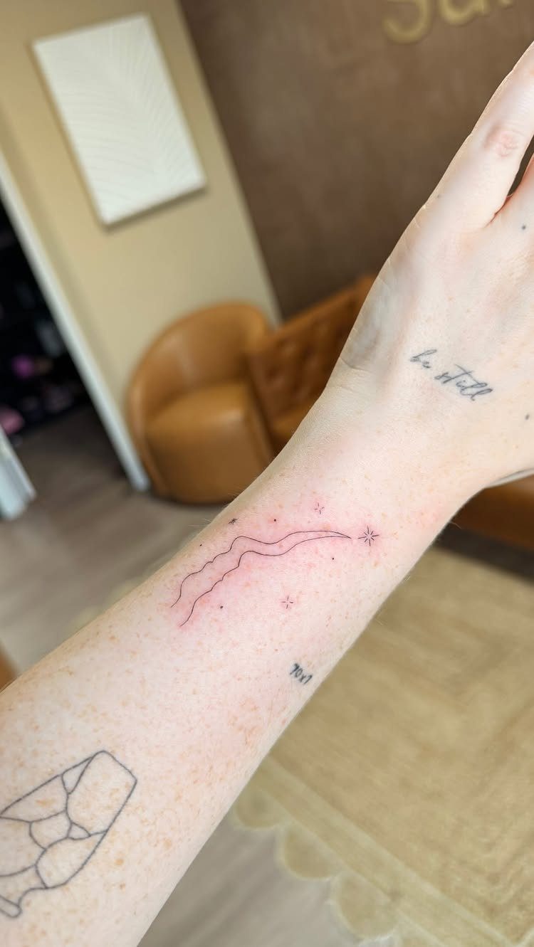 Forearm with a small shooting star tattoo and other minimalist ink designs.