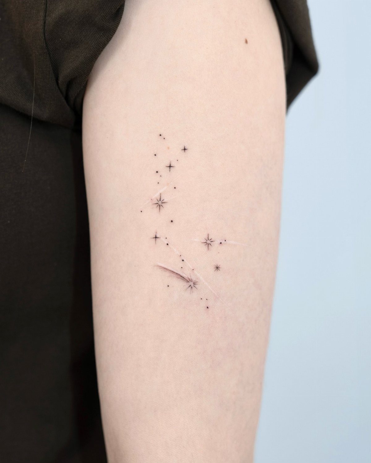 Small black star tattoos scattered on a person's upper arm skin.