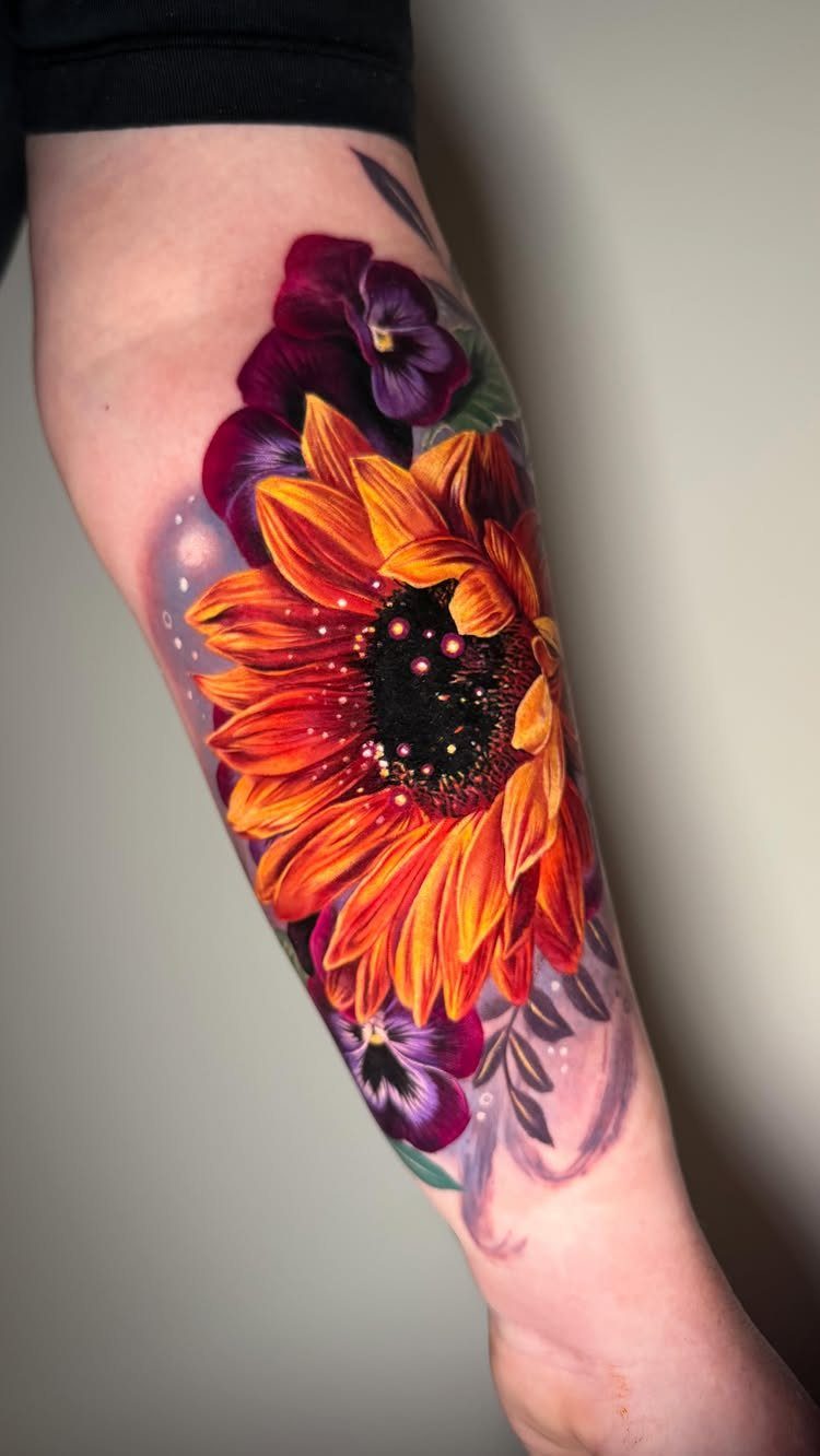 Vibrant sunflower and purple pansy tattoo on a person's lower leg.