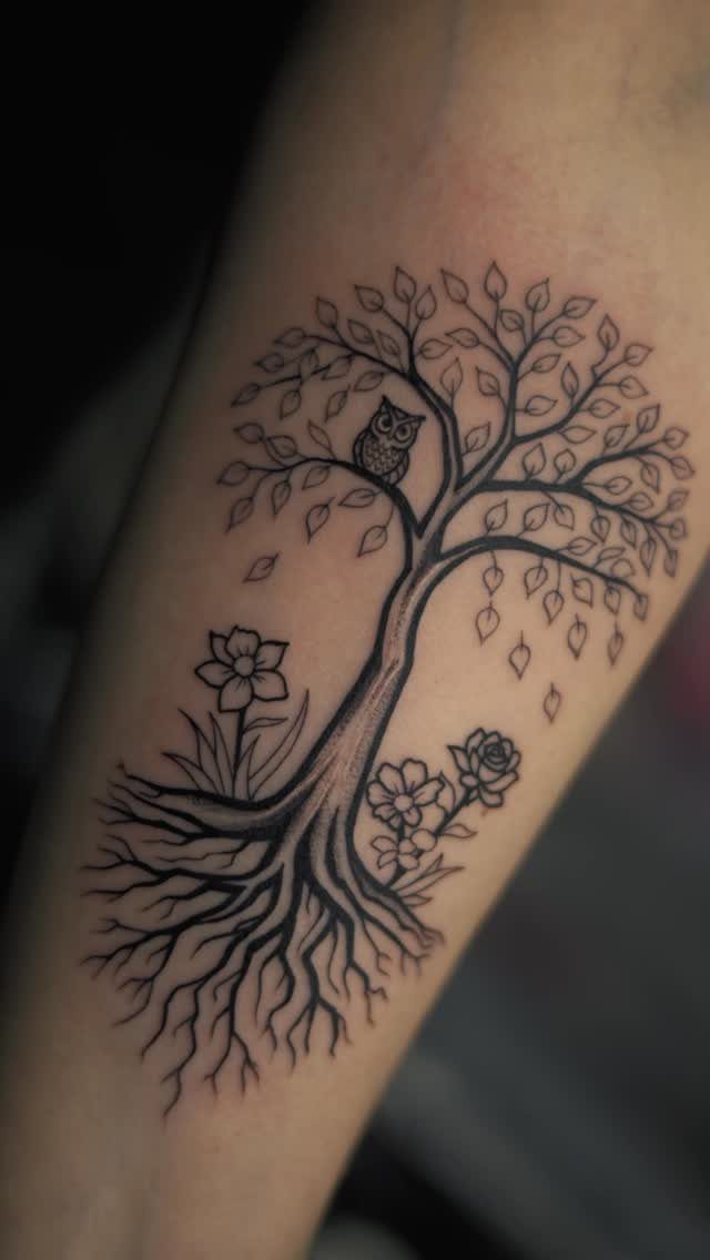 Tree of life tattoo with an owl and flowers on a person's arm.