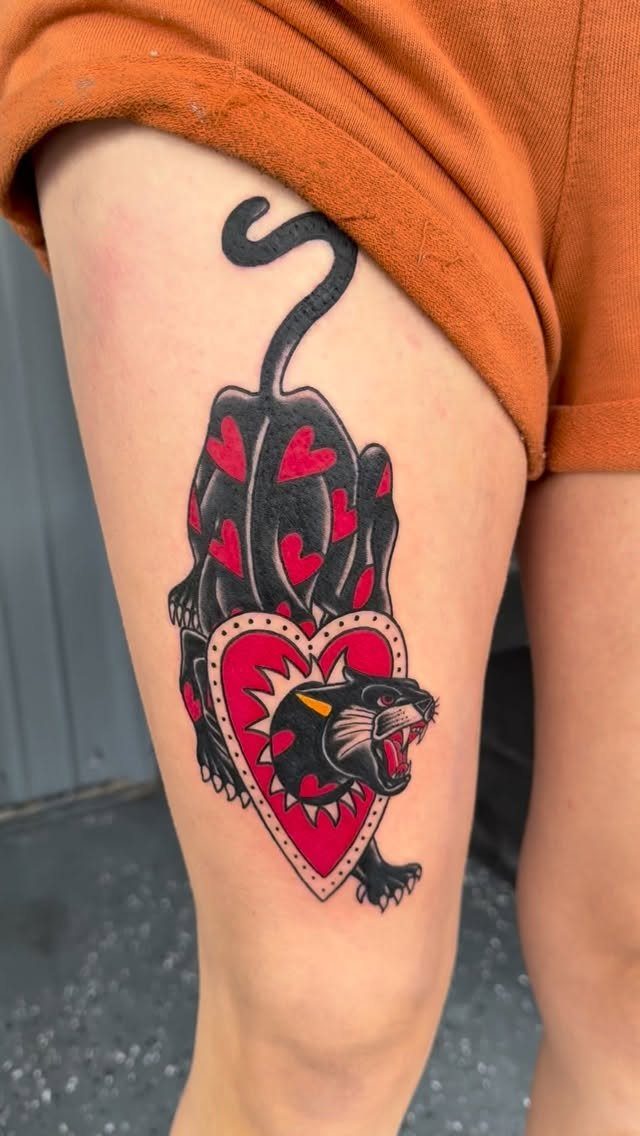 Black panther tattoo with red hearts on a person's thigh in traditional style.