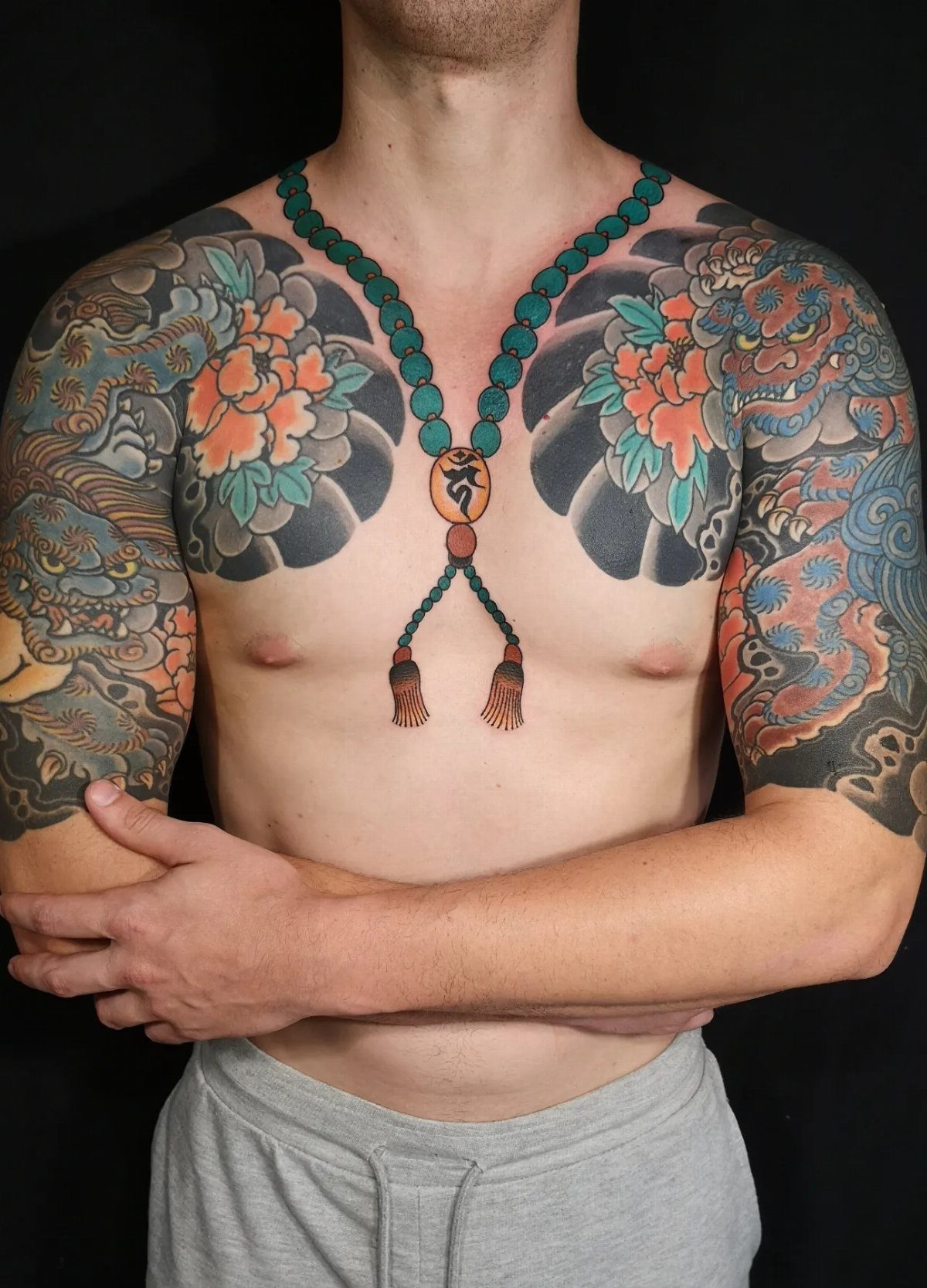 Man with traditional Japanese tattoos on chest and shoulders including orange floral patterns.
