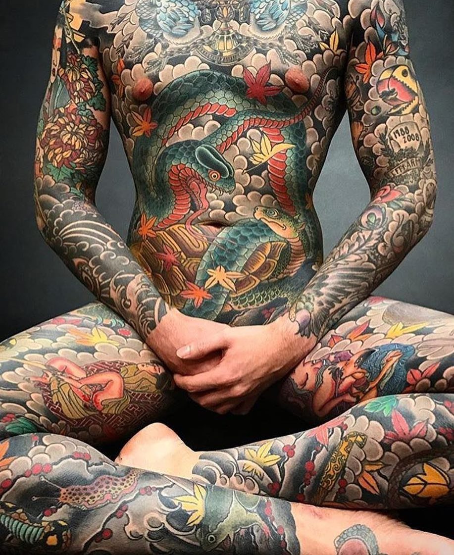 Man with full body traditional Japanese tattoos featuring dragons and colorful waves.