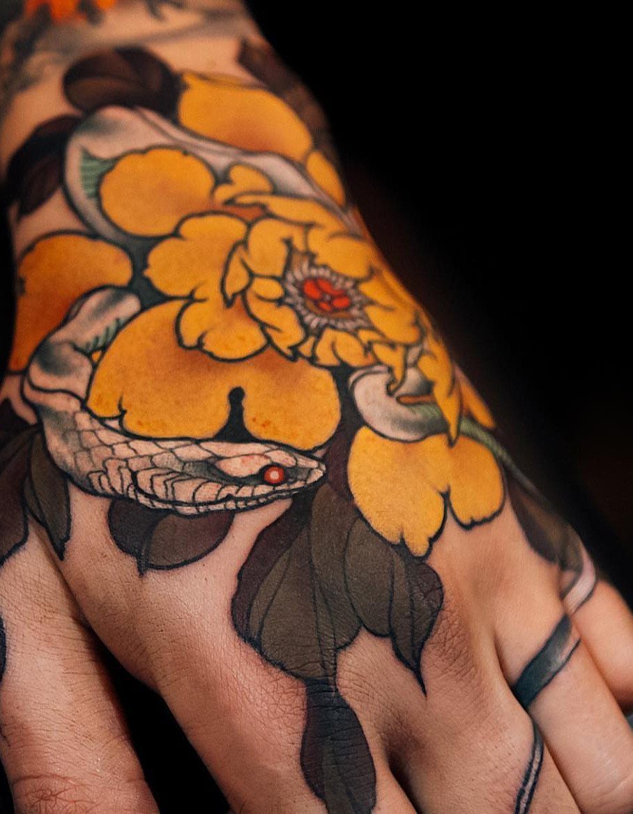 Hand tattoo featuring a yellow peony flower and a white snake in Japanese style