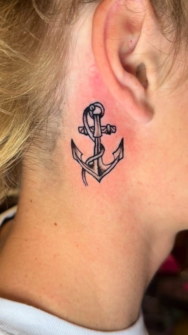 Black ink anchor tattoo with rope on a person's neck behind the ear