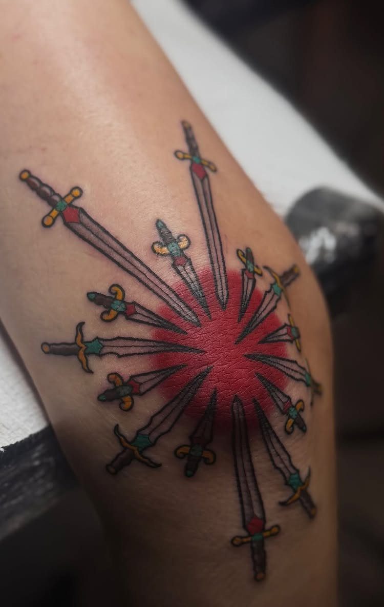 Dagger tattoos pointing toward a red center on a person's skin.