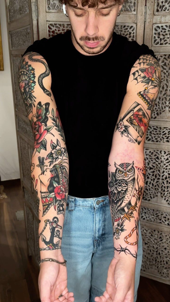 Man with full sleeve traditional tattoos featuring an owl, anchor, and roses.