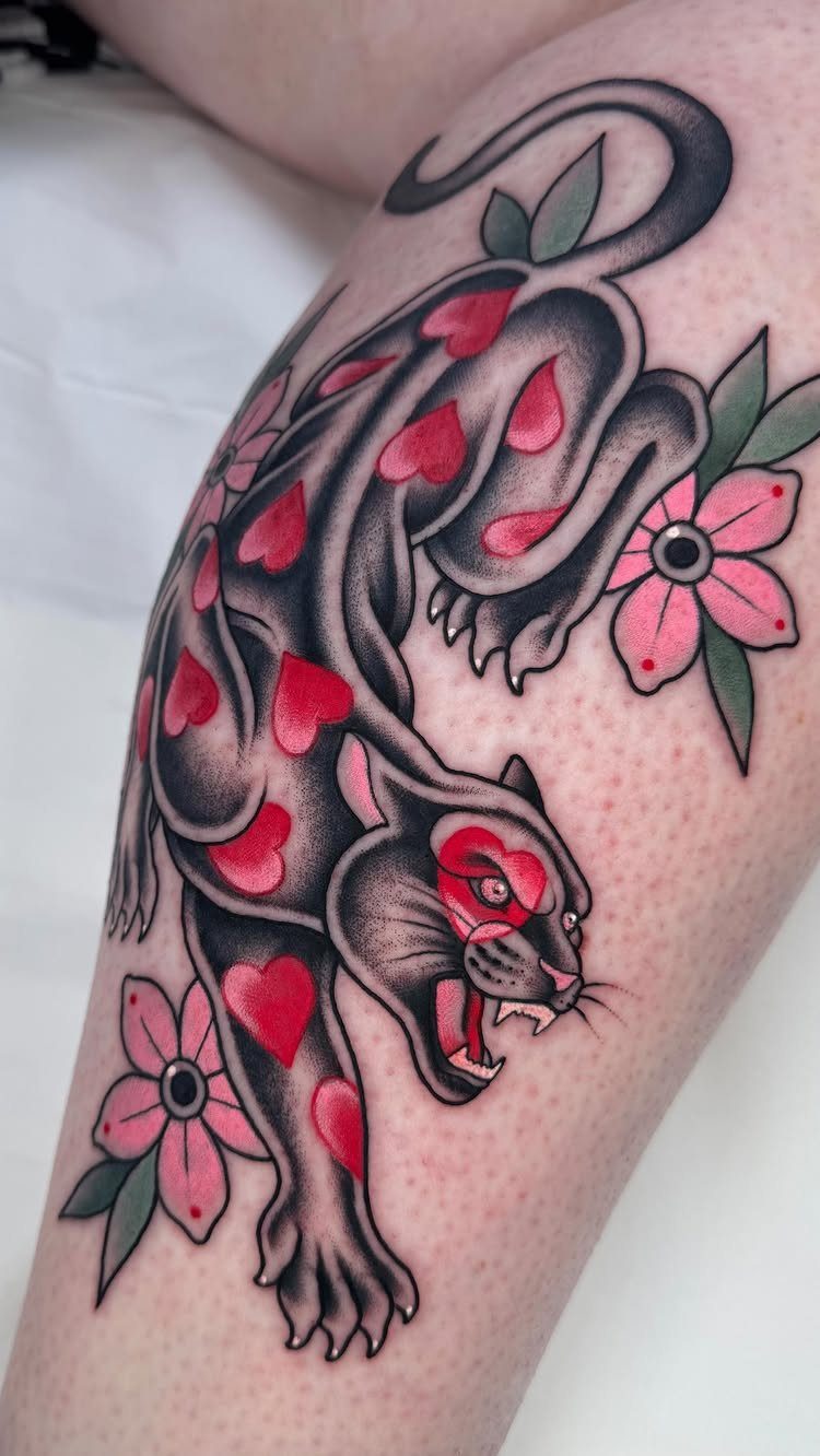 Black panther tattoo with red hearts and pink flowers on human skin.