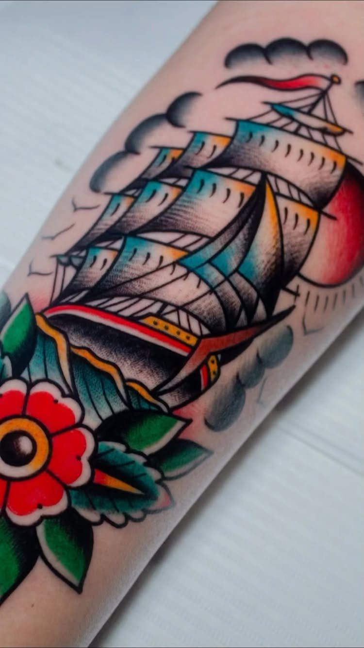 Sailing ship traditional tattoo with bold outlines and a red flower on skin