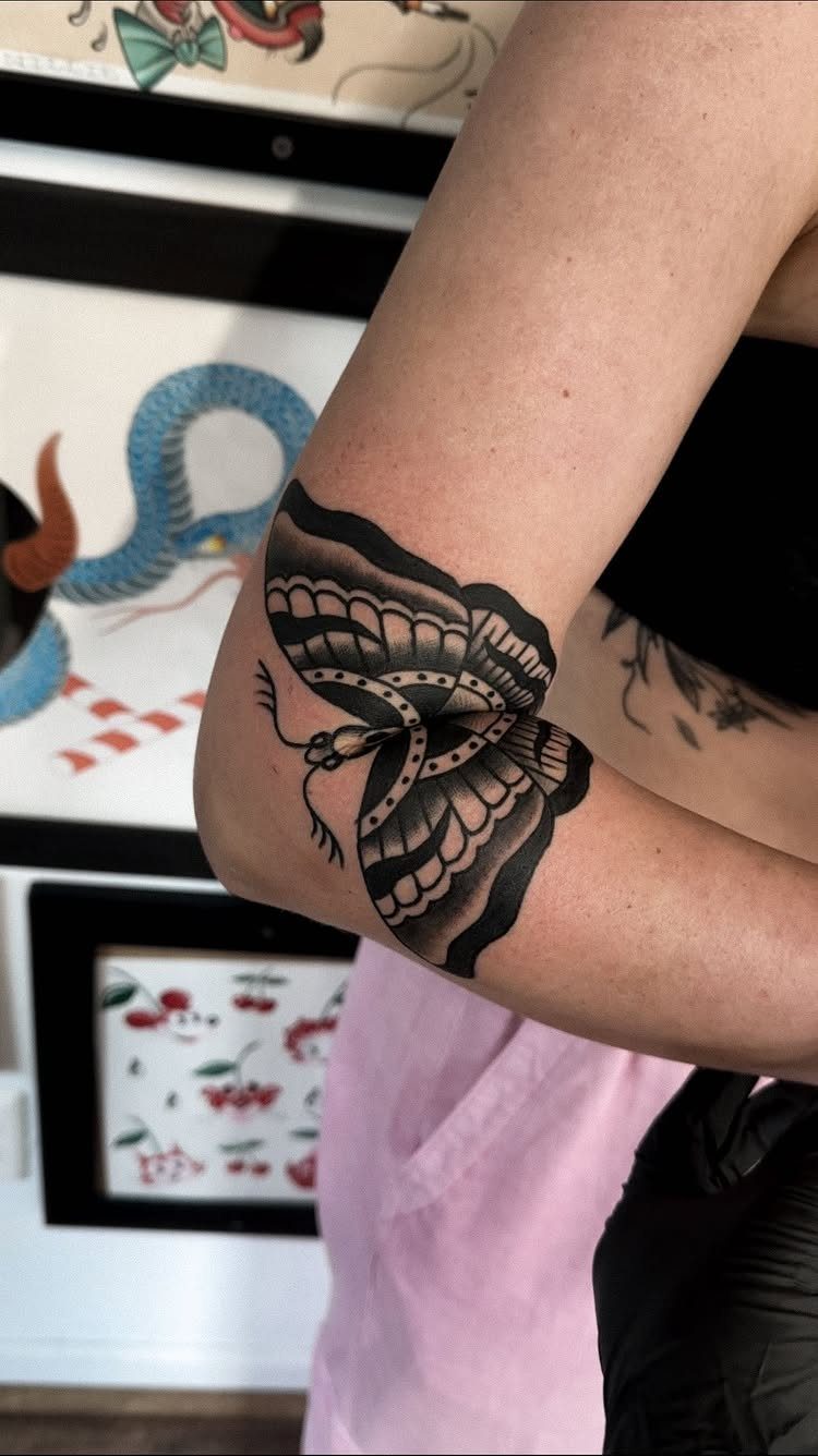 Traditional style butterfly tattoo with bold black shading on a person's elbow