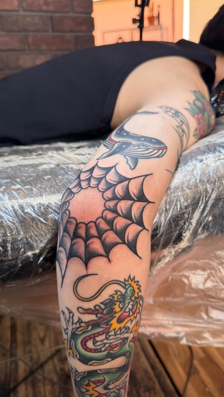 Tattooed arm showing a colorful dragon, spider web, and whale in traditional style.