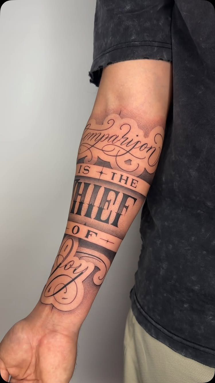 Forearm tattoo with stylized black lettering reading Comparison is the thief of joy