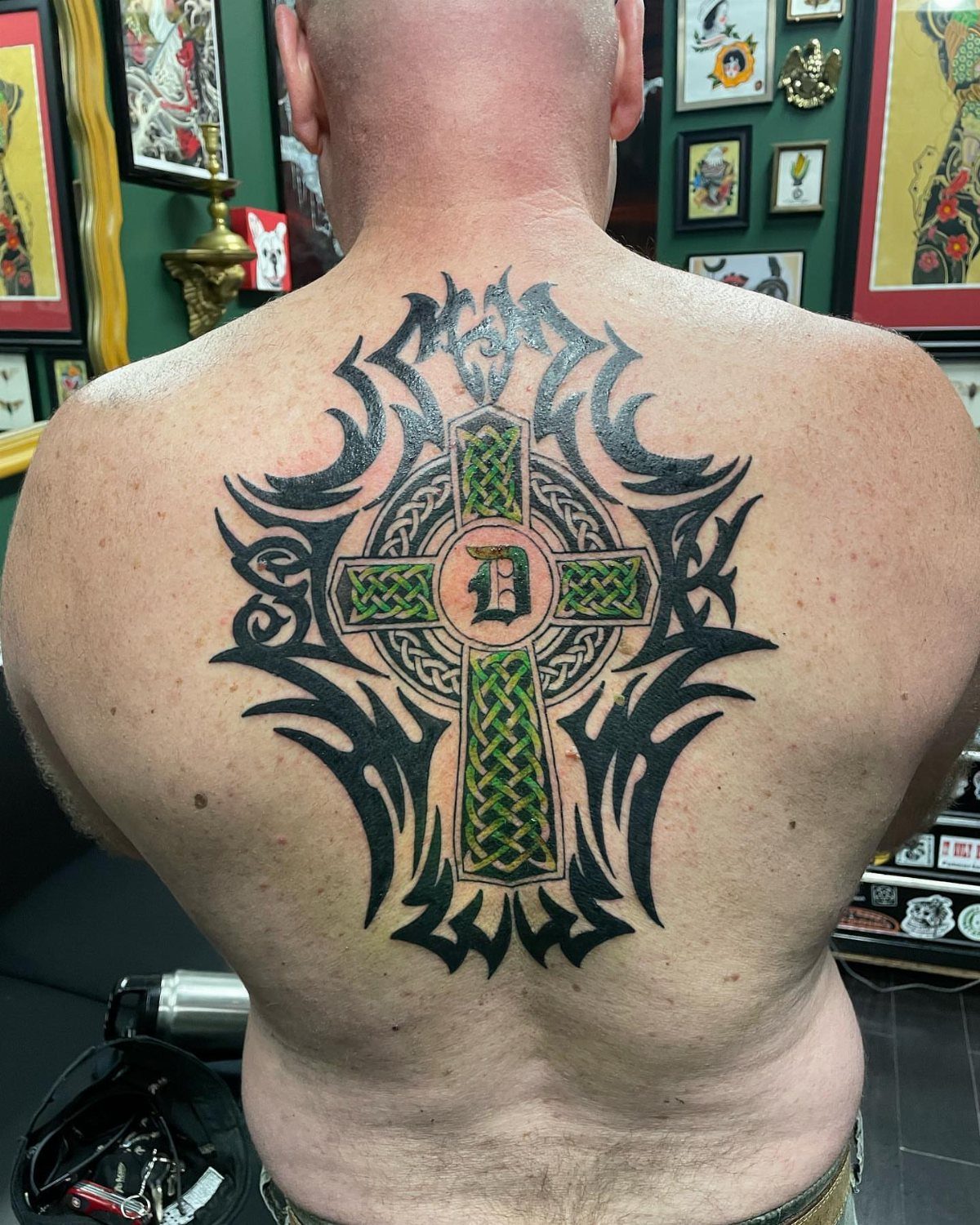 Celtic knot cross tattoo with green ink and black tribal patterns on a back