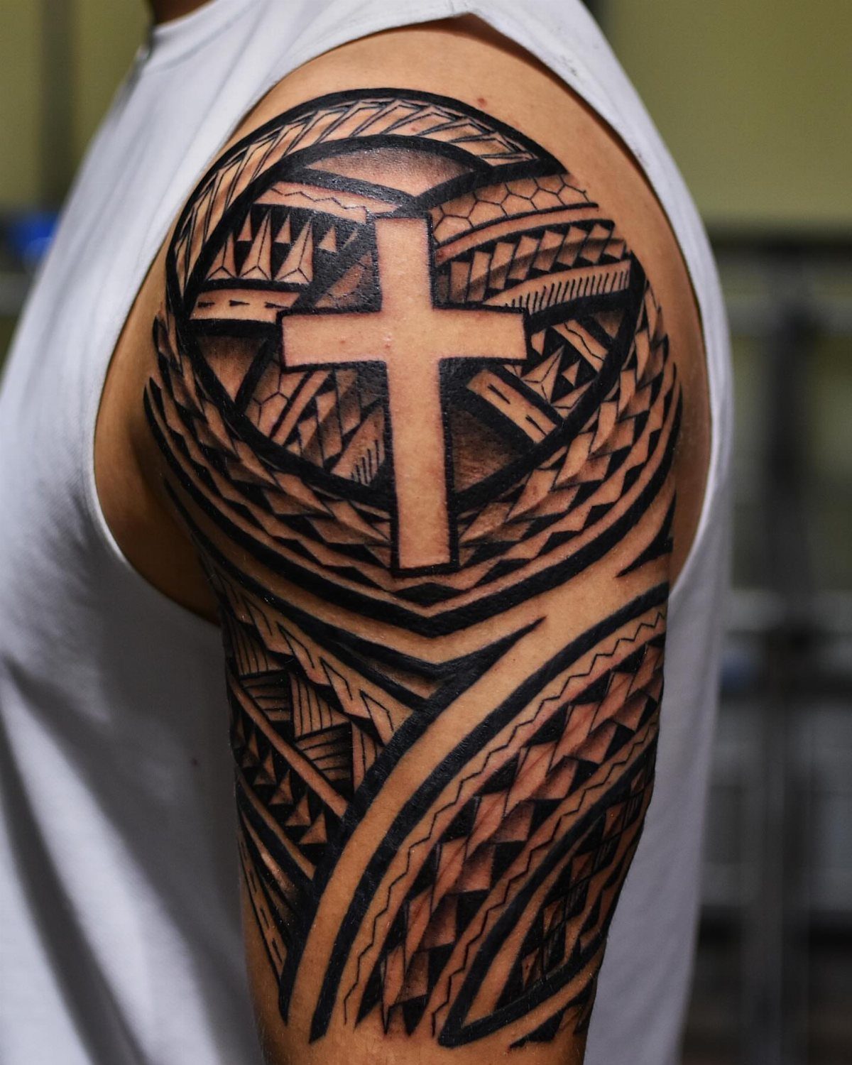 Tribal cross tattoo covering the upper arm and shoulder with geometric black patterns.