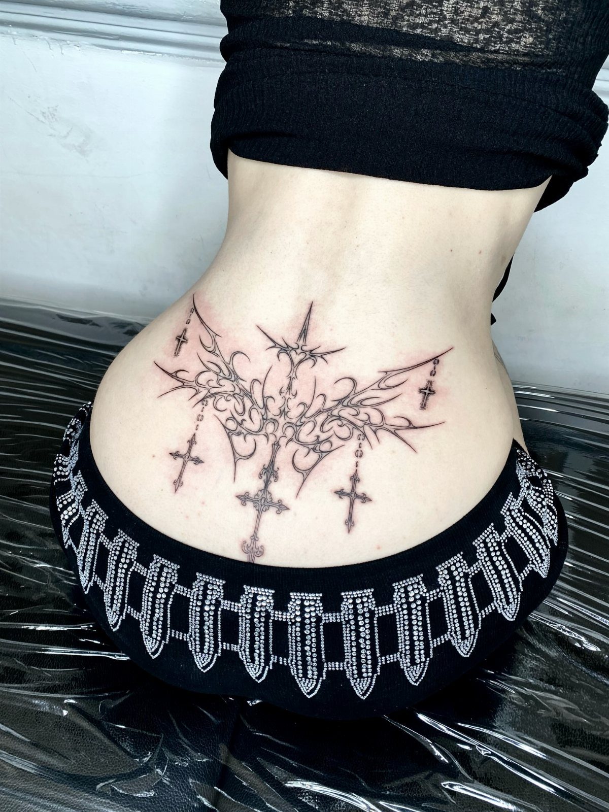 Tribal cross tattoo on a person's lower back with symmetrical black ink designs.