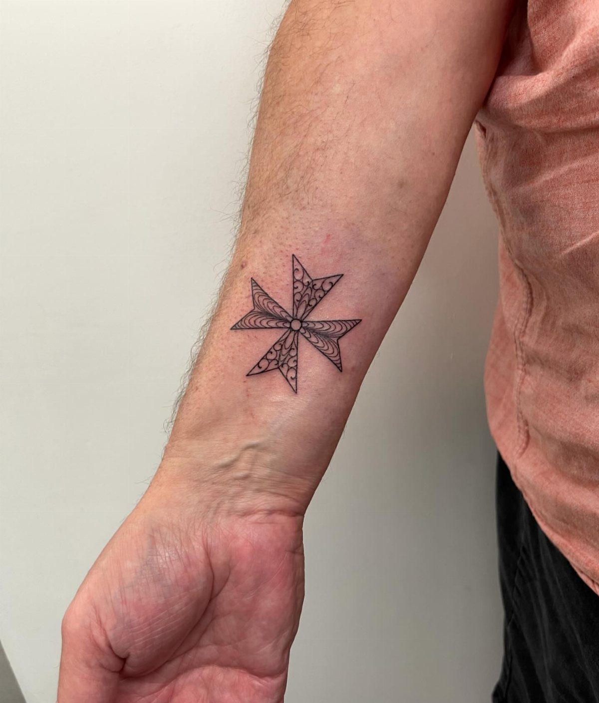 Tribal Maltese cross tattoo on a person's forearm with intricate black ink patterns.