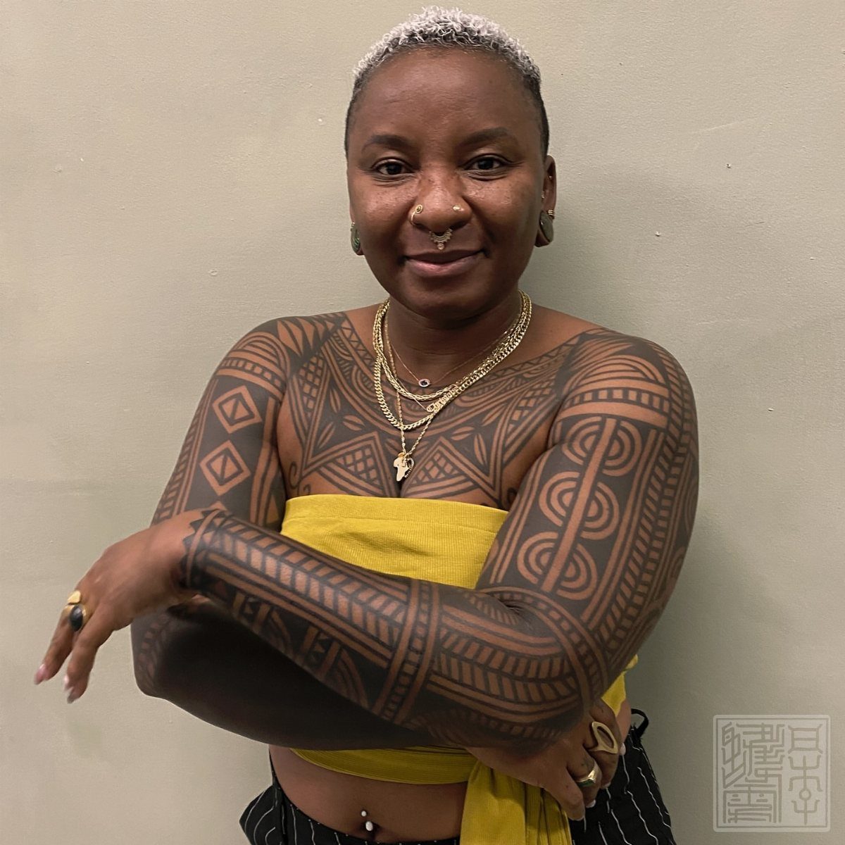 Woman with extensive black geometric tribal tattoos on her chest and arms.
