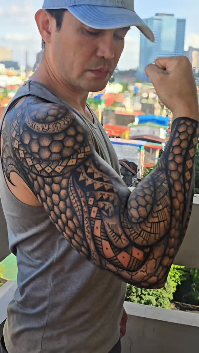 Man posing to show a detailed black ink Filipino tribal tattoo on his arm.