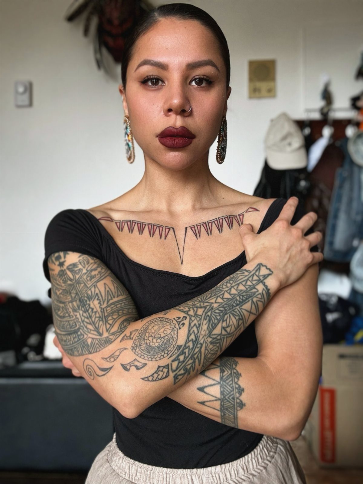 Woman with geometric tribal tattoos on her arms and chest posing indoors.