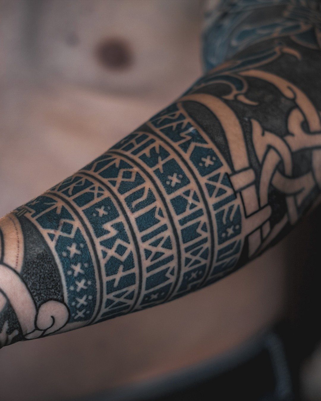 Tattooed arm featuring Norse runes and geometric tribal patterns in black ink.
