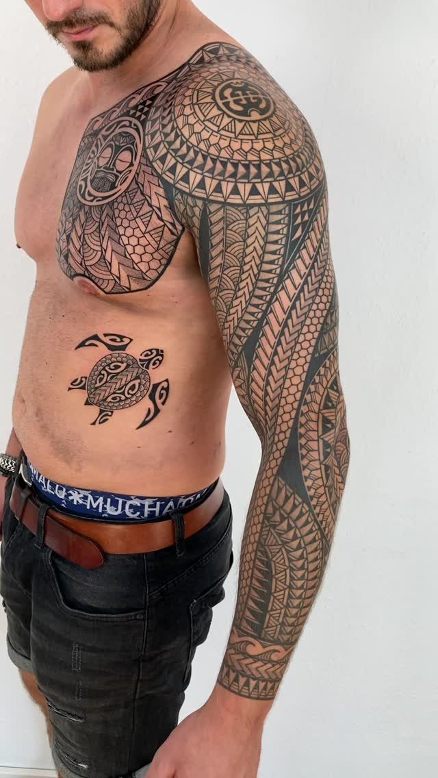 Man with detailed Polynesian tribal tattoos covering his arm, shoulder, and chest.