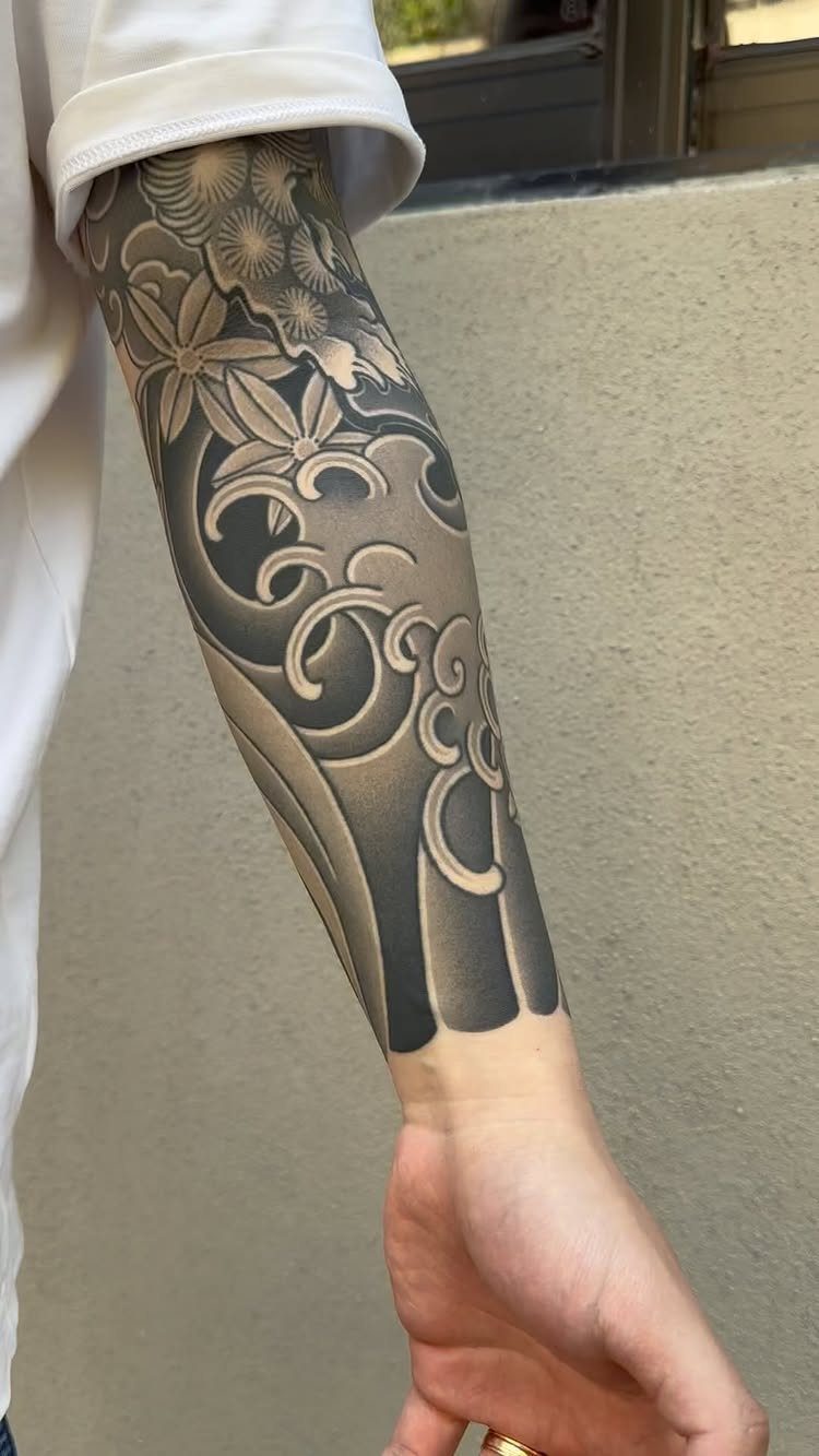 Forearm with a traditional Japanese Irezumi tattoo featuring waves and floral patterns.