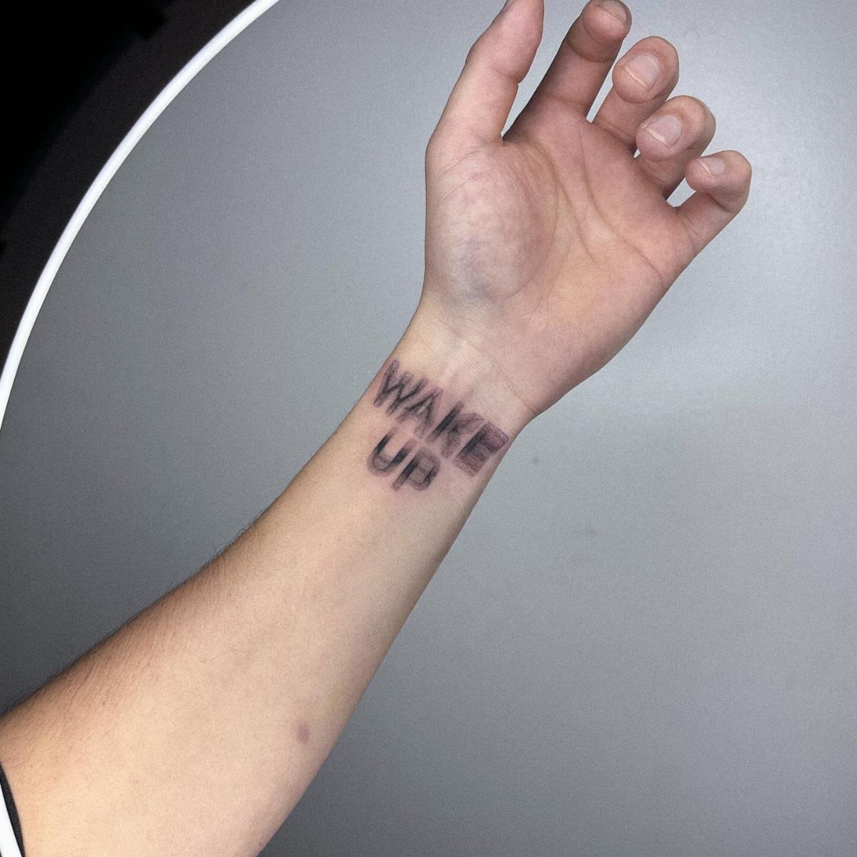 Wrist tattoo with the words WAKE UP in a black typewriter font