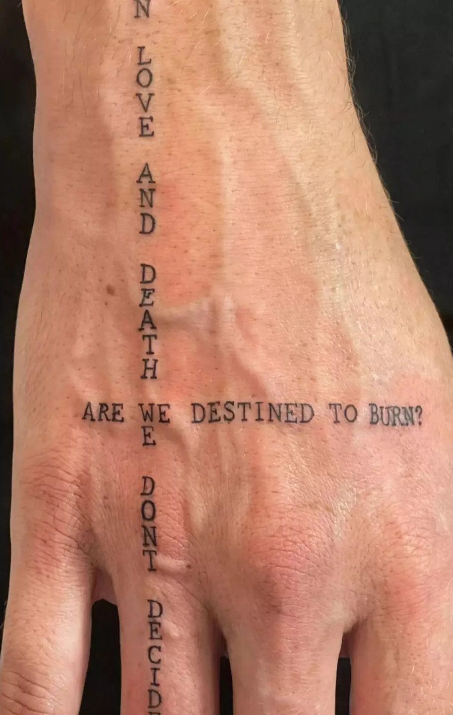 Typewriter font tattoos on a hand and wrist forming a cross shape.