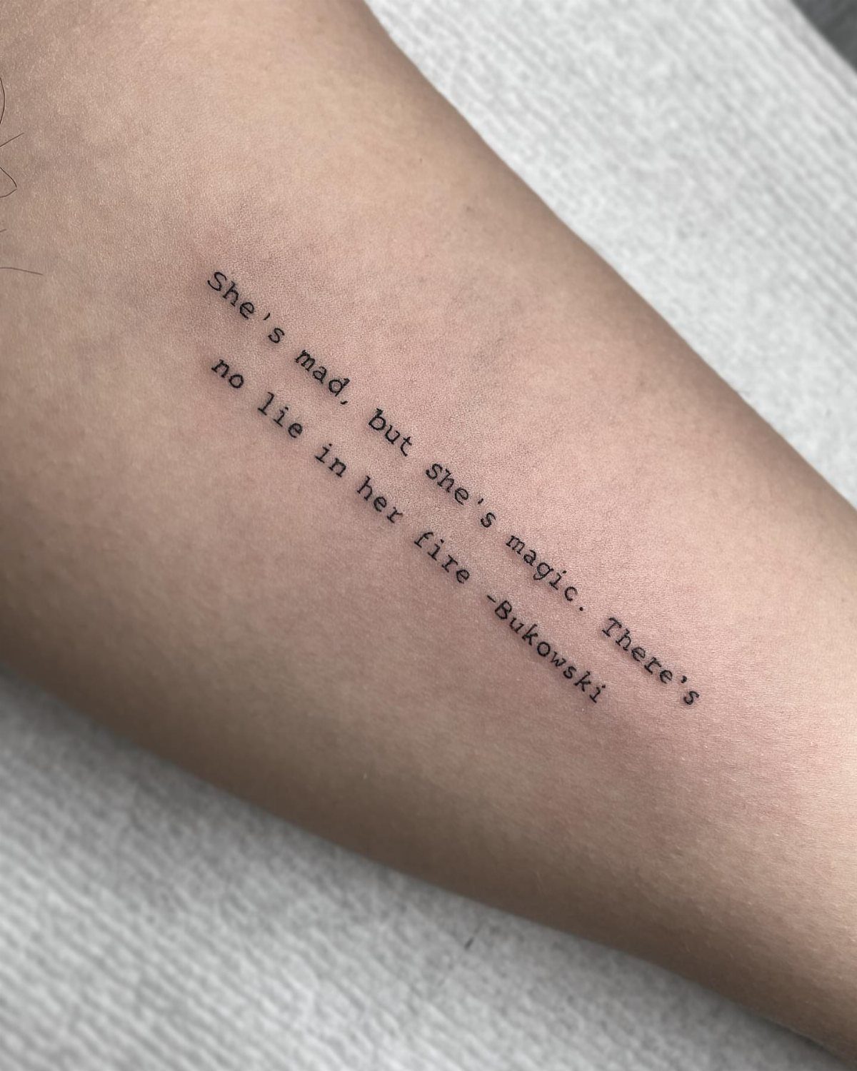 Typewriter font tattoo on a forearm featuring a quote by Charles Bukowski.