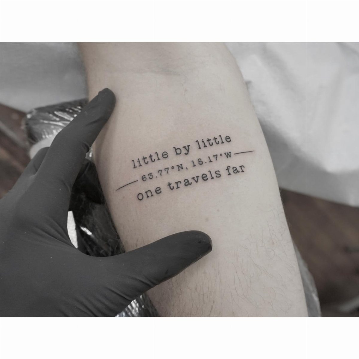 Typewriter font tattoo on a forearm with a quote and geographic coordinates.