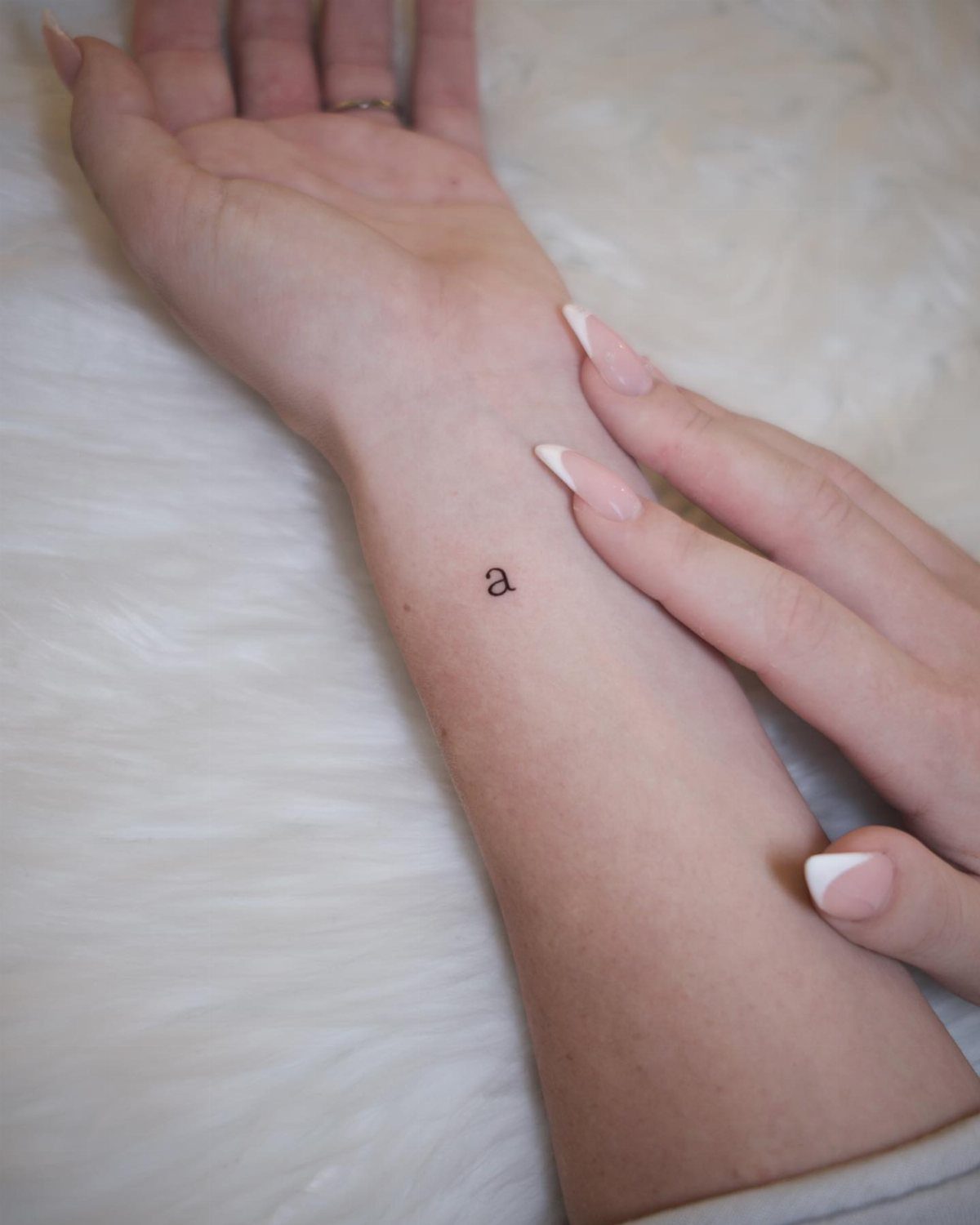 Small lowercase letter a typewriter font tattoo on a person's inner wrist