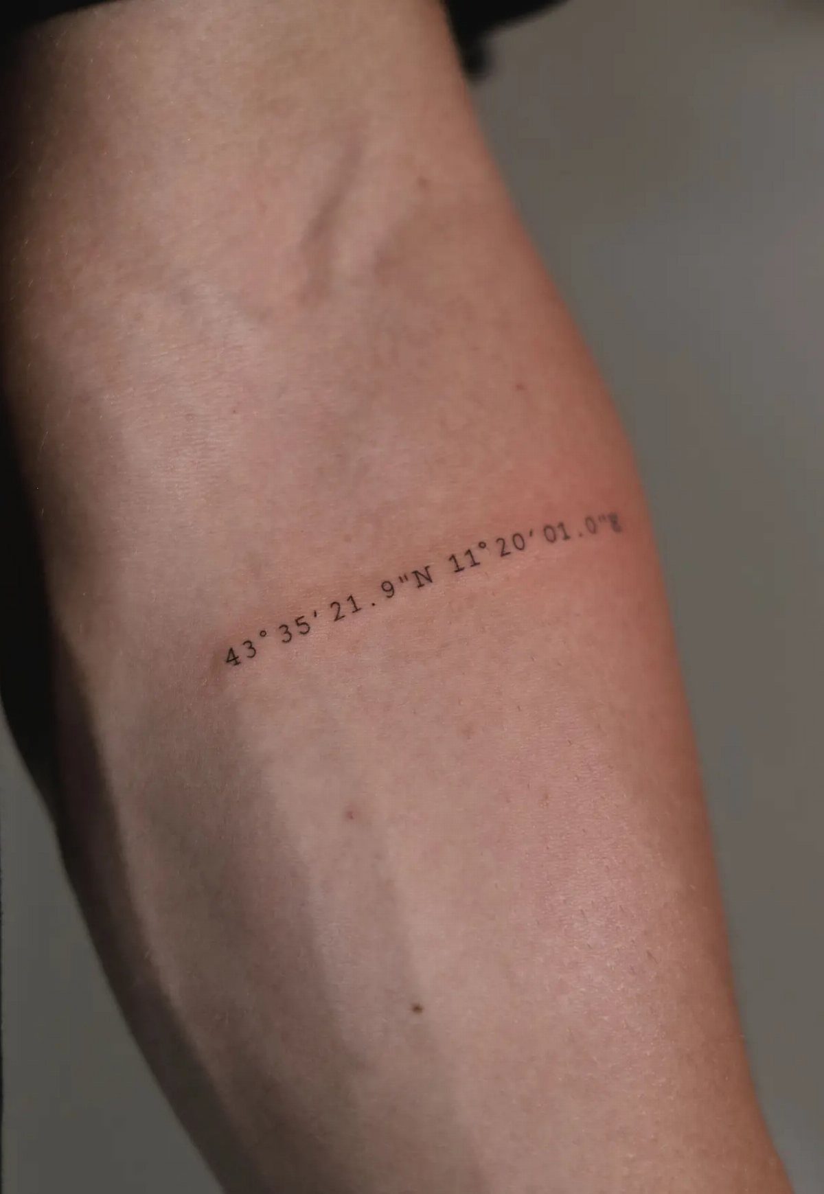 Typewriter font tattoo of geographic coordinates on a person's forearm.