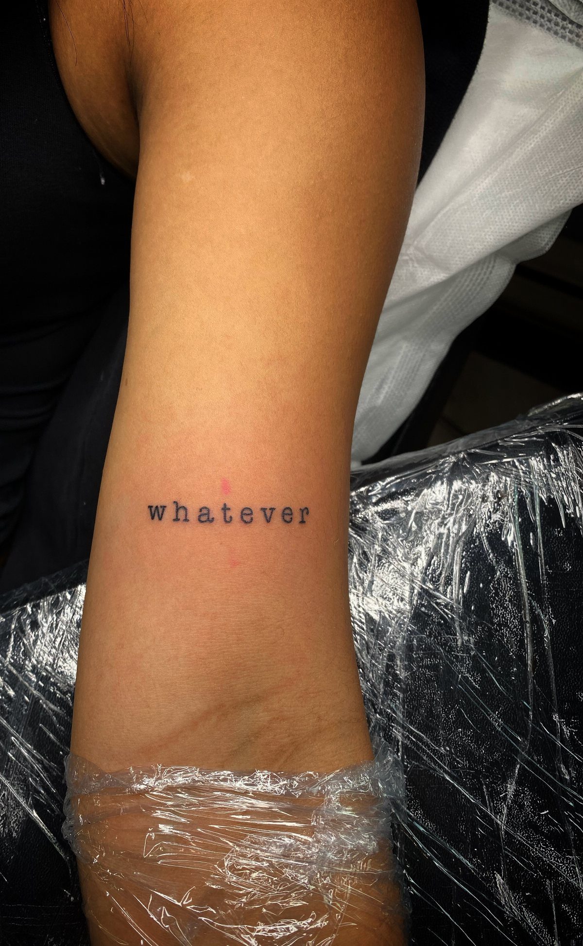 Wrist tattoo with the word whatever written in a black typewriter font