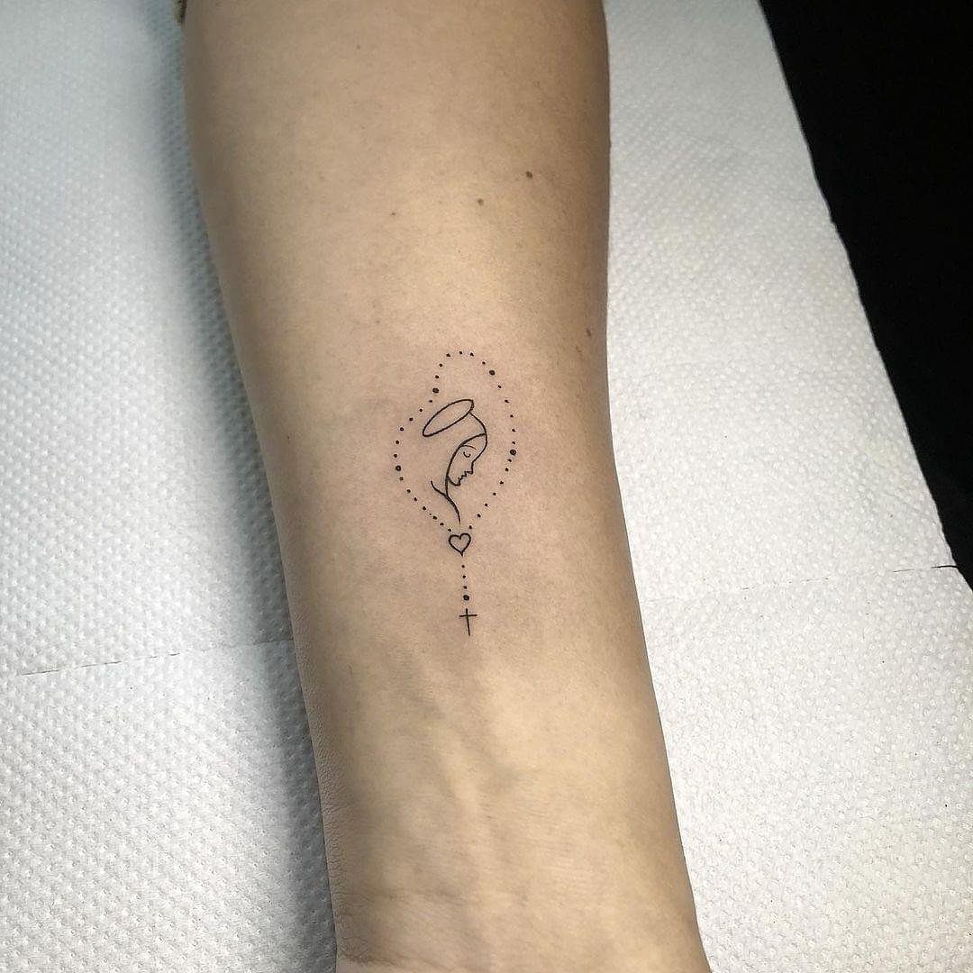 Small minimalist Virgin Mary silhouette tattoo with a halo, heart, and cross.