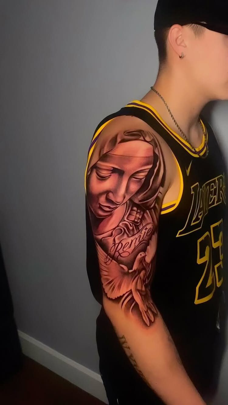 Virgin Mary tattoo on an upper arm featuring a dove and script text.