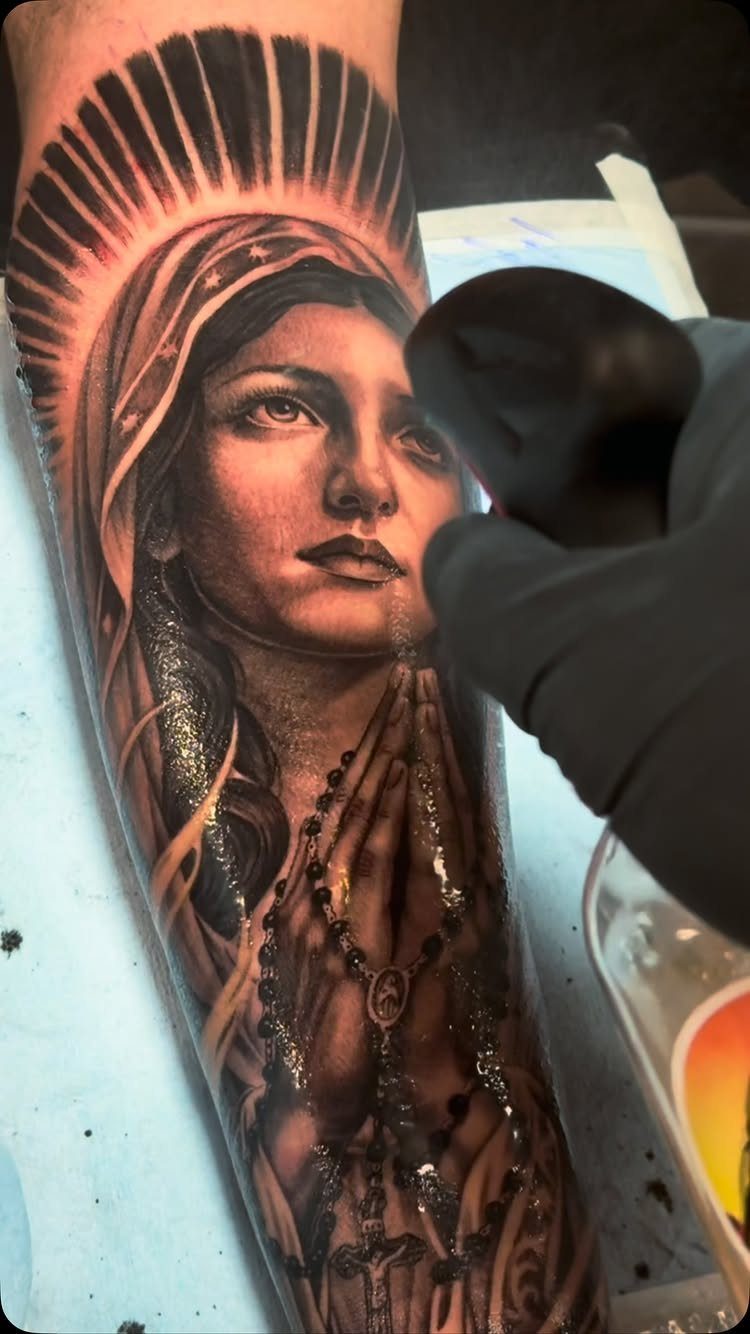 Virgin Mary tattoo with rosary and halo on a person's arm.